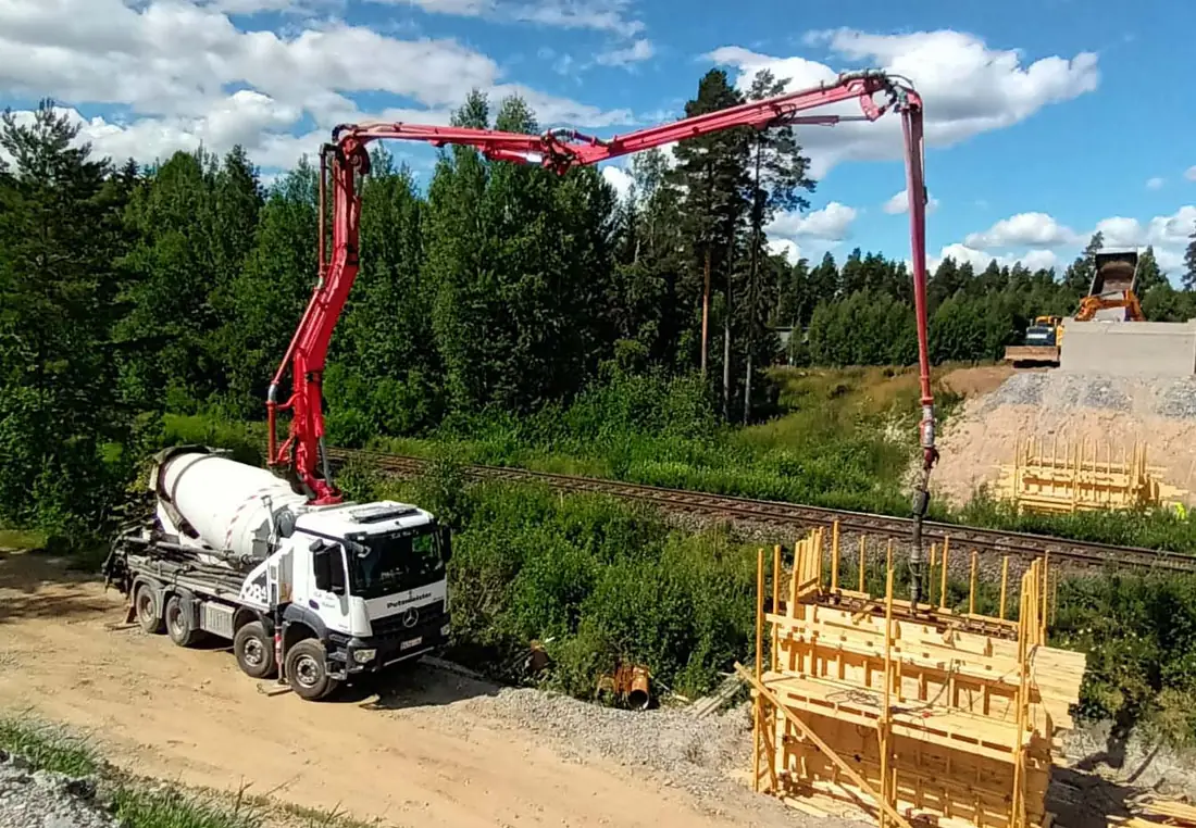 Betonipumppu valaa muottia 28-metrisellä puomilla kesäisellä työmaalla radan varressa